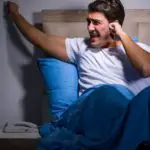 image of man in bed knocking wall due to noise from neighbor