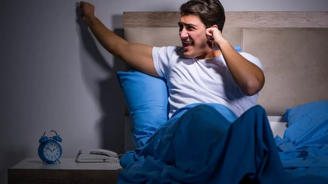 image of man in bed knocking wall due to noise from neighbor